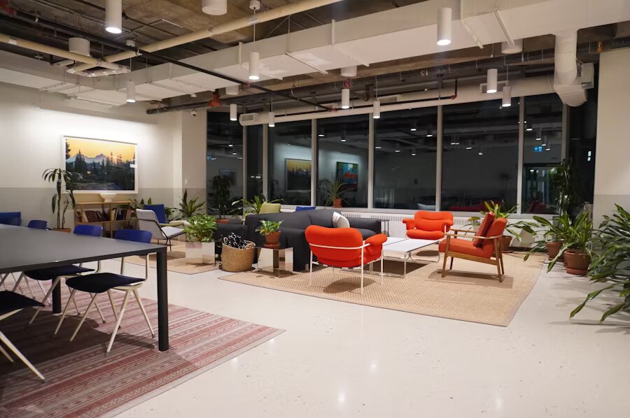 Spazio lounge accogliente con poltrone arancioni e blu, piante ornamentali, decorazioni moderne e illuminazione soffusa in un ambiente aperto